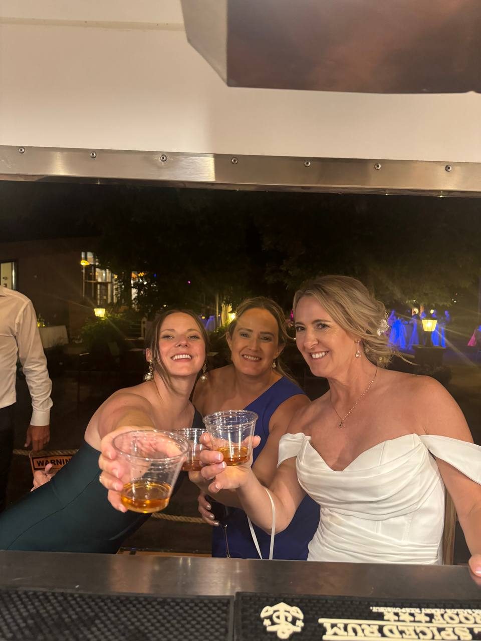 Guests raising a toast at the bar, including a bride in a white gown