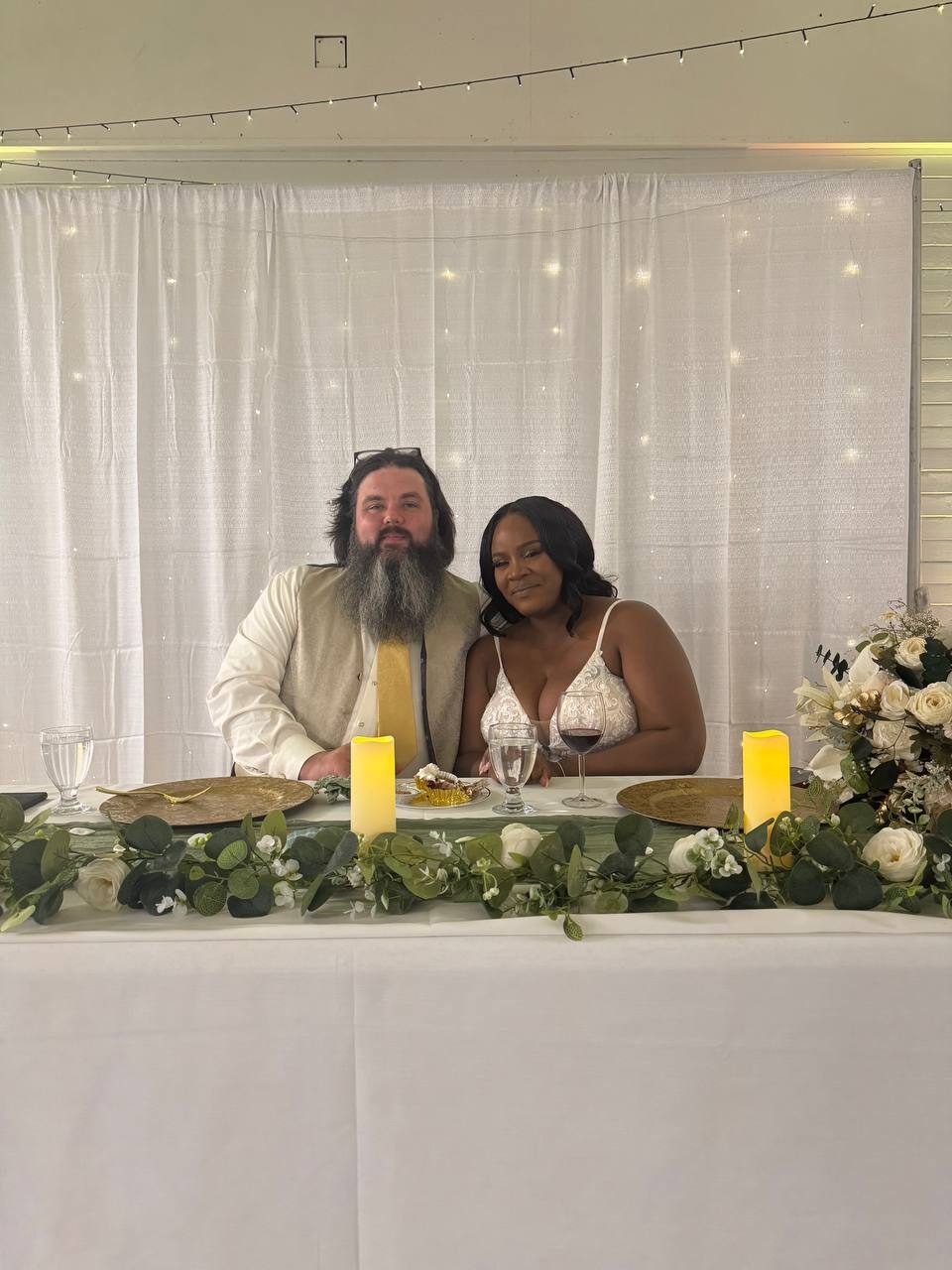 Newlyweds seated at the head table with candles and greenery