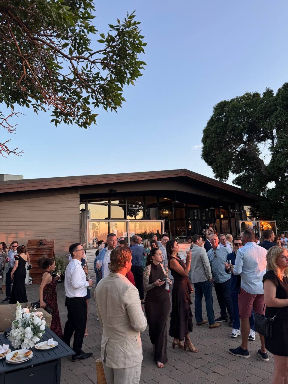 Wedding guests mingling on a patio at sunset with drinks in hand